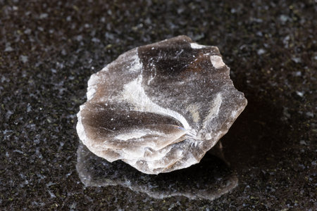 sample of rough obsidian rock (volcanic glass) on black granite background close up from Armeniaの写真素材