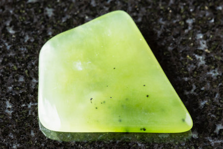 sample of polished light green nephrite rock on black granite background close up from Sayan...