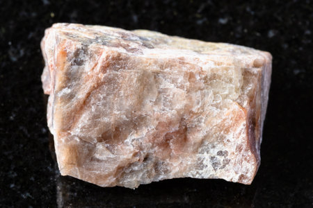 sample of unpolished nepheline mineral on black granite background close up from Southern Urals, Russiaの写真素材