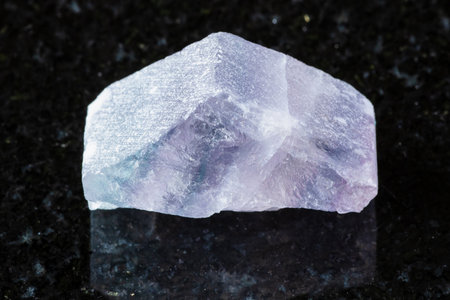 sample of rough purple striped fluorite mineral on black granite background close upの写真素材