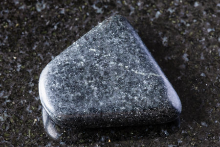 sample of tumbled dolerite rock on black granite background close up from Karelia, Russia