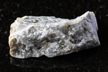 sample of raw melilite (melilite-monticellite metasomatite) rock on black granite background close...