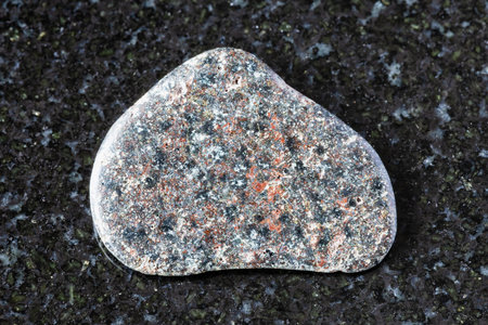 sample of tumbled basalt with hematite mineral on black granite background close up from Karelia,...