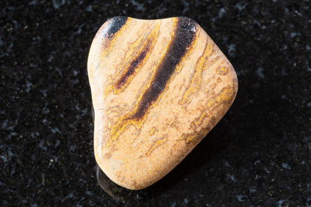 sample of polished tuff (tuffaceous) sandstone mineral on black granite background close up from...