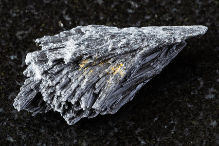 sample of raw black kyanite mineral on black granite background close up