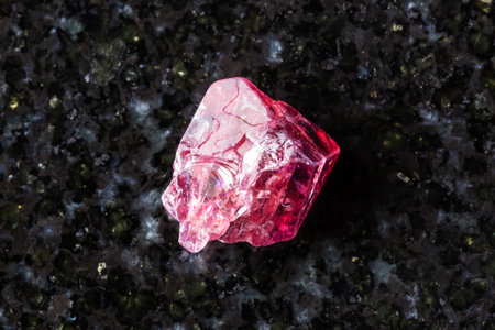 sample of rough red spinel crystal on black granite background close up