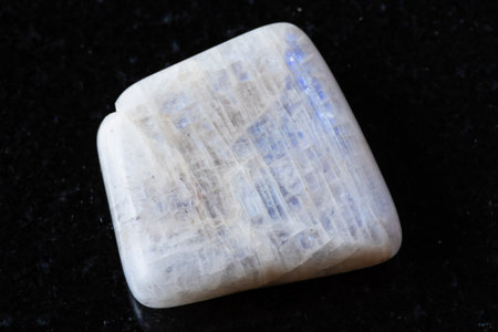 sample of tumbled belomorite moonstone mineral on black granite background close upの写真素材