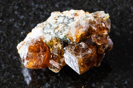 sample of raw hessonite grossular rock on black granite background close up from Middle Urals, Russiaの写真素材