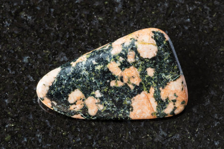 sample of tumbled gabbro mineral on black granite background close up from Karelia, Russiaの写真素材