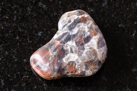 sample of tumbled monzonite mineral on black granite background close up from Irkutsk region, Russiaの写真素材