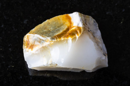 sample of raw white opal mineral on black granite background close up