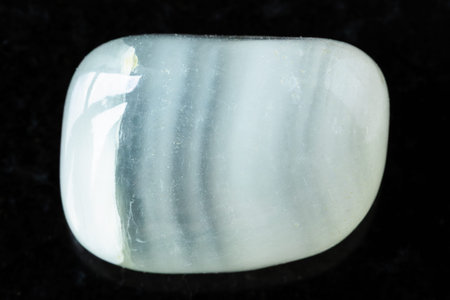 sample of tumbled colorless calcite mineral on black granite background close up from Argentina