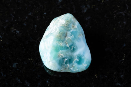 sample of rough larimar mineral on black granite background close up from Dominicana