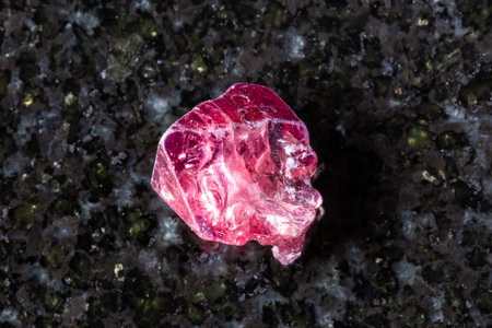 sample of raw red spinel crystal on black granite background close up from Myanmar