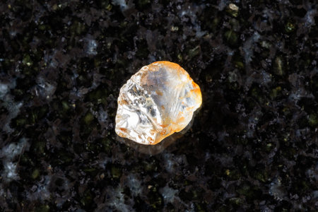 sample of raw colorless sapphire mineral on black granite background close up from Madagascar