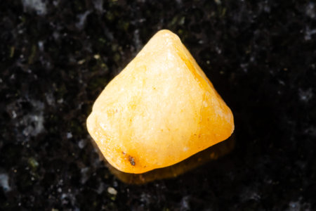 sample of raw yellow sapphire crystal on black granite background close up from Myanmar