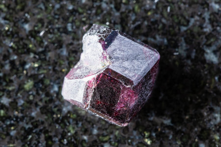 sample of raw single rhodolite pyrope crystal on black granite background close up