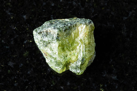 sample of rough green sphene mineral on black granite background close up from Pakistan