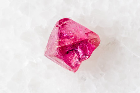 sample of raw pink spinel mineral on white marble background close up