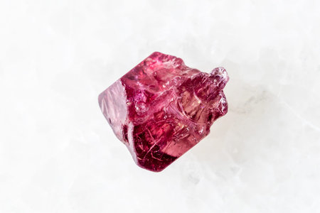 sample of raw red spinel crystal on white marble background close up