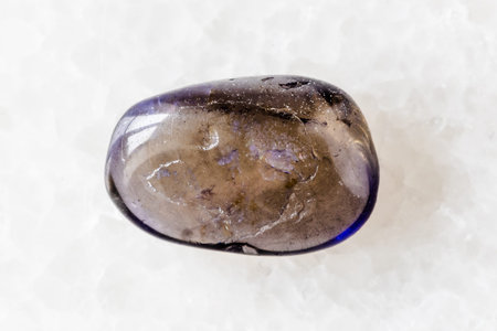sample of tumbled iolite mineral on white marble background close up
