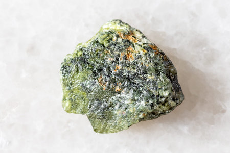 sample of unworked green sphene mineral on white marble background close up from Pakistan