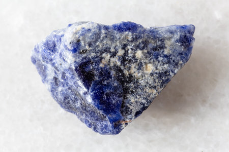 sample of raw sodalite rock on white marble background close up