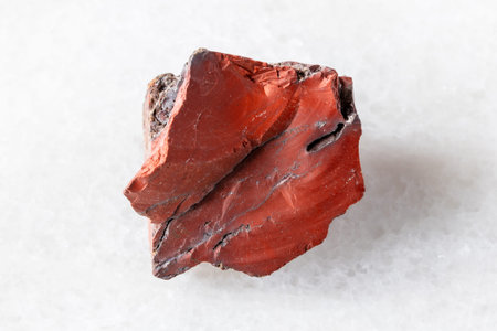 sample of raw red mookaite mineral on white marble background close up
