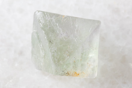 sample of single rough fluorite crystal on white marble background close up