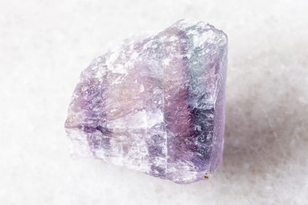 sample of raw purple striped fluorite mineral on white marble background close up