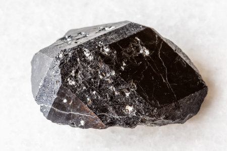 sample of rough melanite andradite black garnet crystal on white marble background close up from...