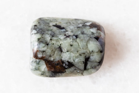 sample of tumbled khibinite rock on white marble background close up