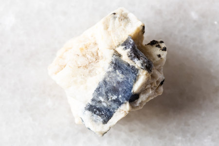 sample of blue corundum sapphire in raw rock on white marble background close up