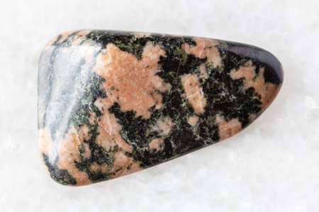 sample of polished gabbro rock on white marble background close up from Karelia, Russia