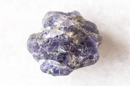 sample of raw iolite mineral on white marble background close up