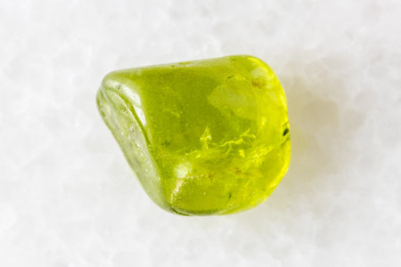 sample of polished peridod crystal on white marble background close up