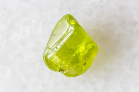 sample of tumbled peridod crystal on white marble background close up