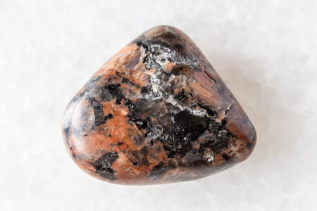 sample of polished granosyenite rock on white marble background close up from Leningrad region,...