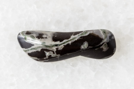 sample of tumbled hornfels mineral on white marble background close up