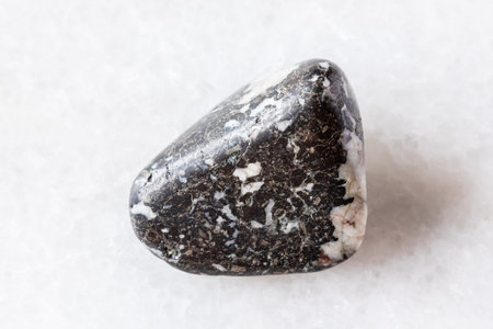 sample of tumbled trachybasalt rock on white marble background close up from Polar Urals, Russia