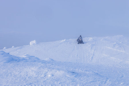 travel to Murmansk Oblast of Russia in winter season - snowmobile drives at snow-covered hill slope near Kandalaksha town in foggy winter dayの写真素材