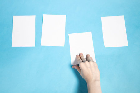 top view of hand takes sheet of white papers on blue paper background