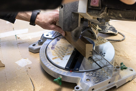 carpenter saws baseboard on portable circular saw in room during apartment renovation