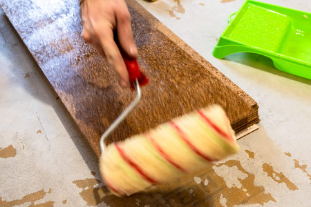 worker applies glue to surface of cork tile with roller in room during apartment renovationの写真素材