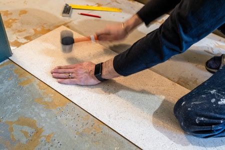 worker glues flooring with plastic hammer in room during apartment renovationの写真素材