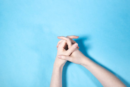 above view of two hands with interlaced fingers on blue paper background