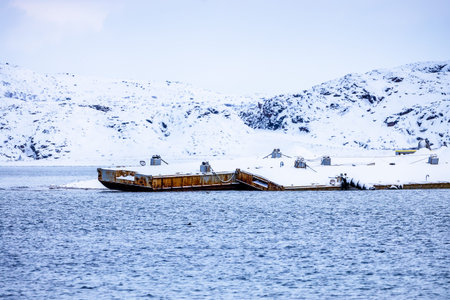travel to Murmansk Oblast of Russia in winter season - snow-covered pier on Barents Sea coast in Teriberka village on overcast winter dayの写真素材