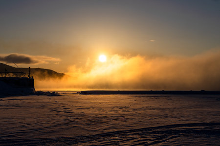travel to Murmansk Oblast of Russia in winter season - view of sunrise over frozen surface of Kandalaksha bay near White Sea embankment in Kandalaksha town at winter morningの写真素材