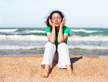 Young happy girl listening to music with headphones while sitting on the beachの写真素材