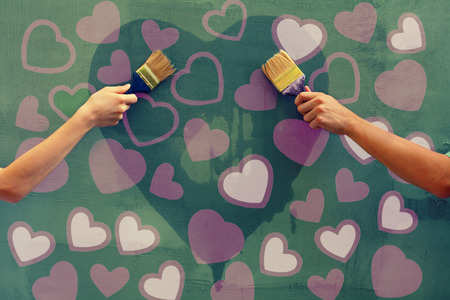 Young man and woman painting hearts on the concrete wallの写真素材